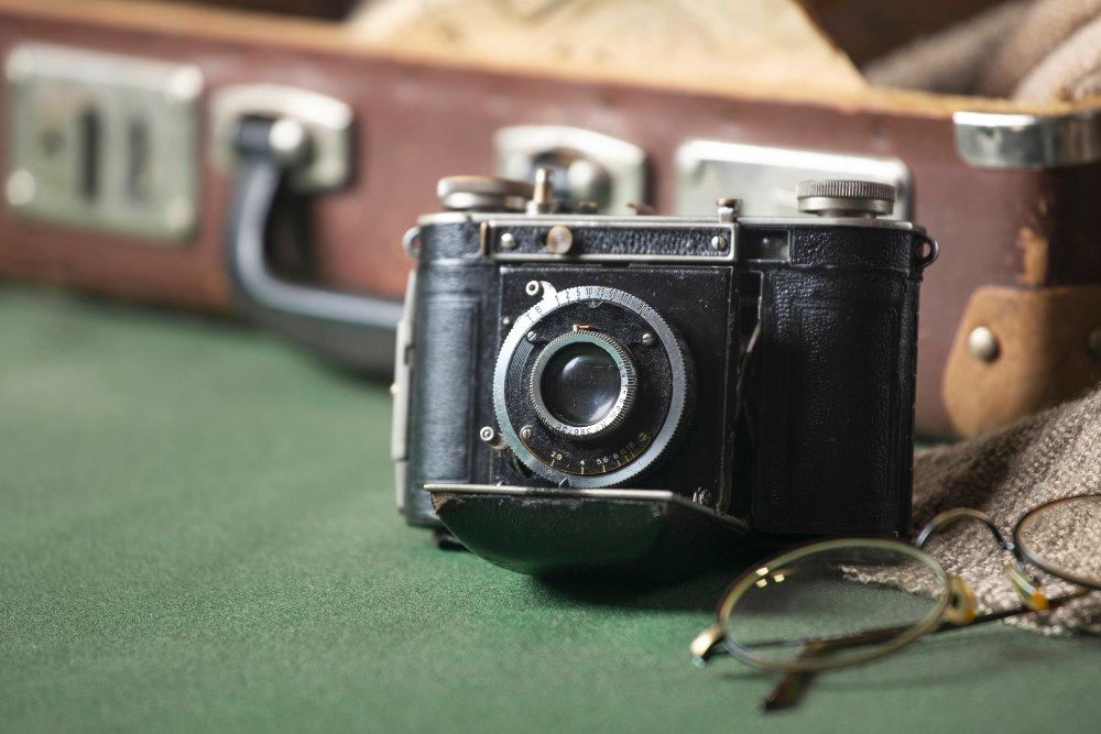 НА фото старовинний антикварний фотоаппарат лежить на фоні старовинного чемодану. Він лежить на зеленому сукні стола.